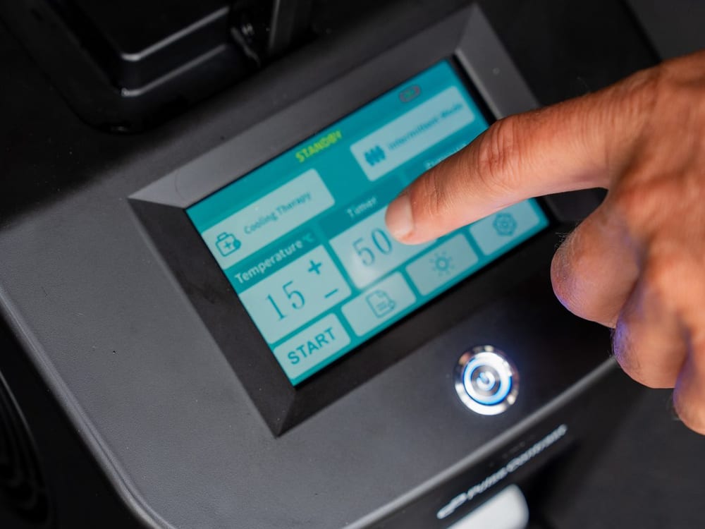 A finger on the unit's touchscreen, showing the cooling therapy, temperature, timer and pressure controls